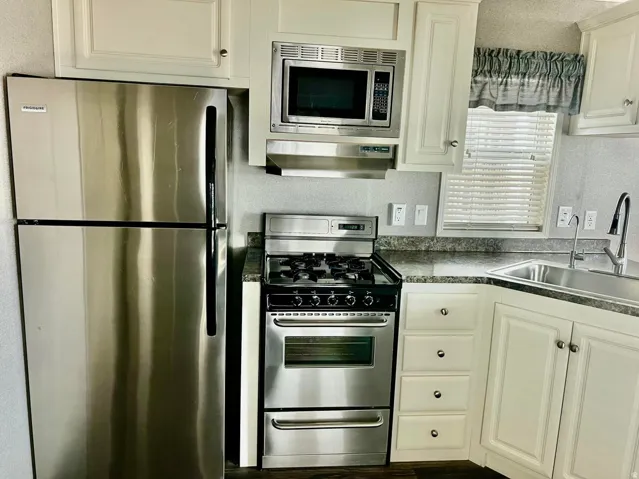 Stainless steel refrigerator, stainless steel gas range, stainless steel microwave, white cabinetry, and a stainless steel sink with a high-arch faucet