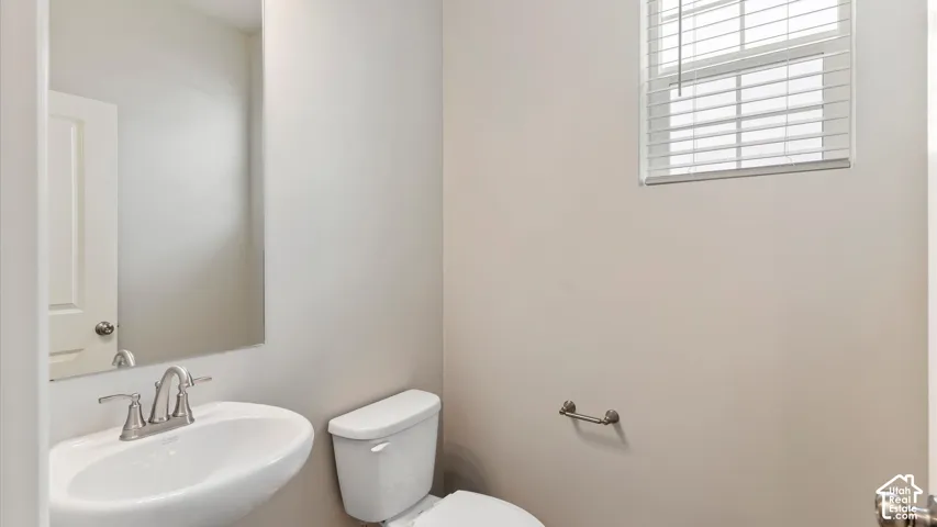 Pedestal sink with a chrome faucet, wall-mounted mirror, and a window with blinds