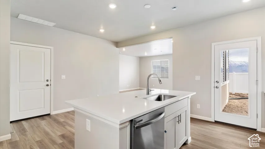 Kitchen island featuring a stainless steel sink with a high-arc faucet, integrated dishwasher, and white countertop