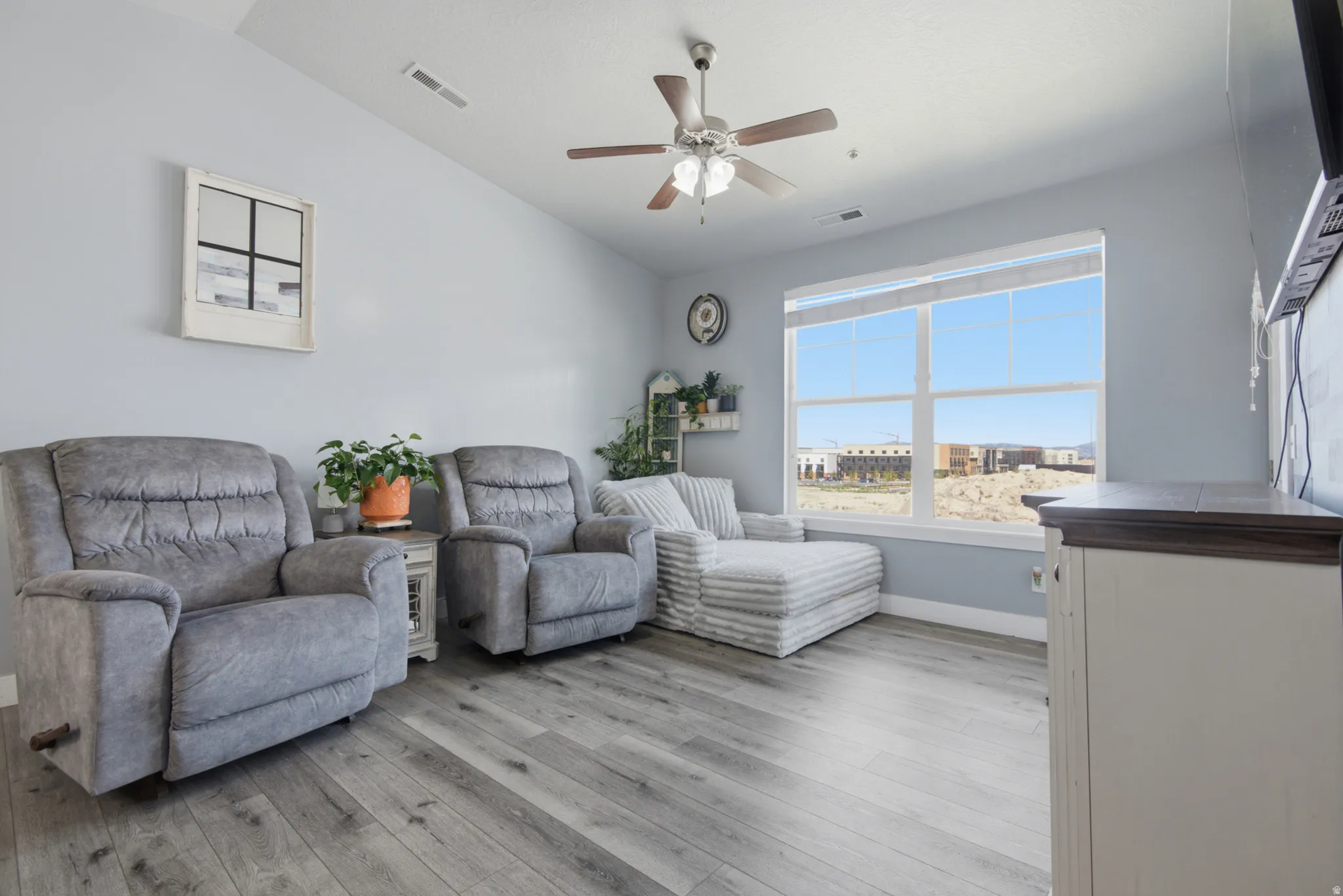 Spacious living area featuring wood-finish flooring, a large window, and a ceiling fan with integrated lighting