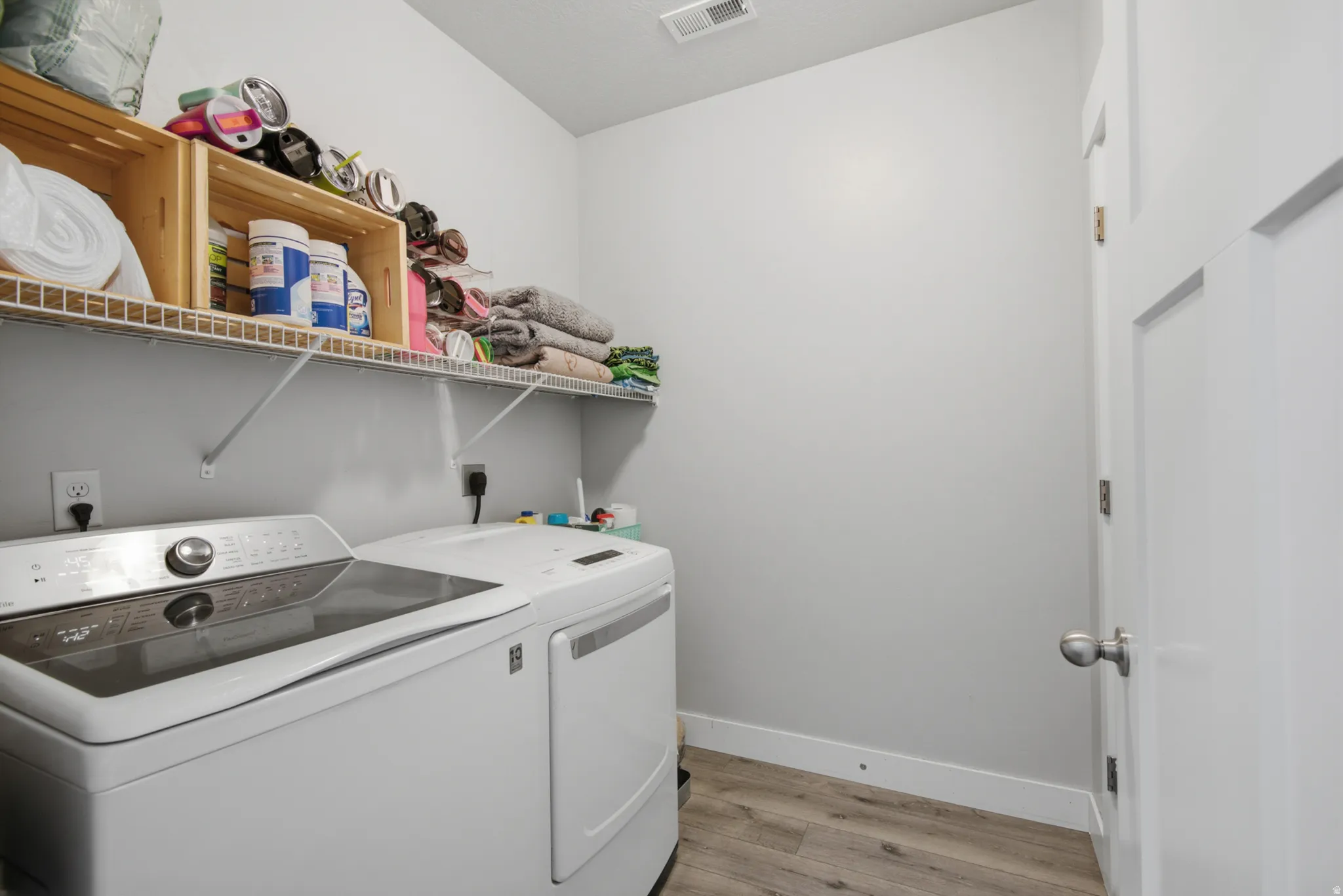 Dedicated laundry room featuring side-by-side washer and dryer appliances, wire shelving with ample storage capacity, wood-finish upper cabinetry, and wood-look plank flooring throughout
