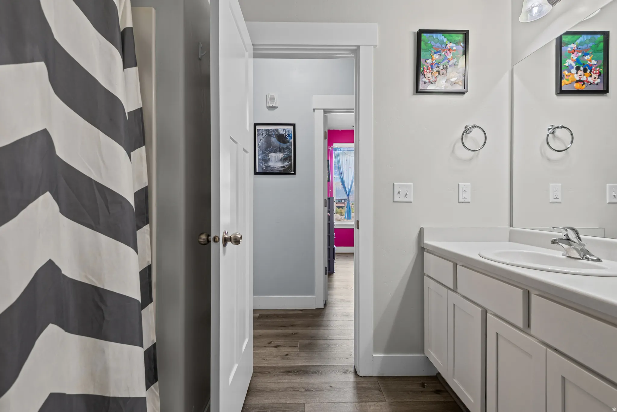 Bathroom featuring a single vanity with white cabinetry, integrated sink, and wood-finish flooring