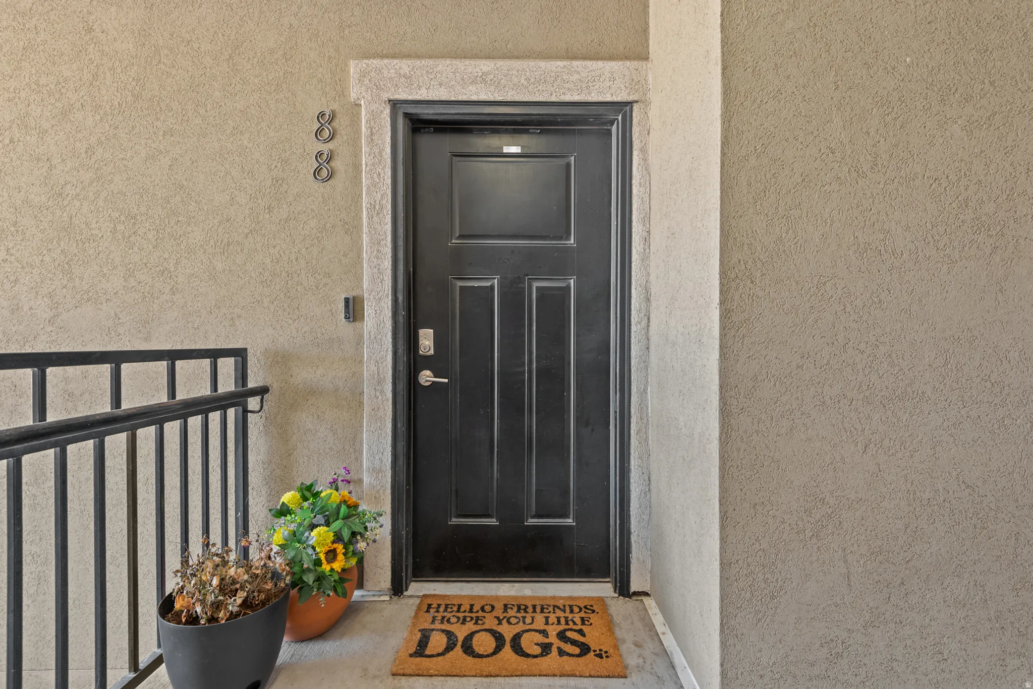 Black paneled entry door with chrome hardware, complemented by a textured stucco exterior and a black metal railing