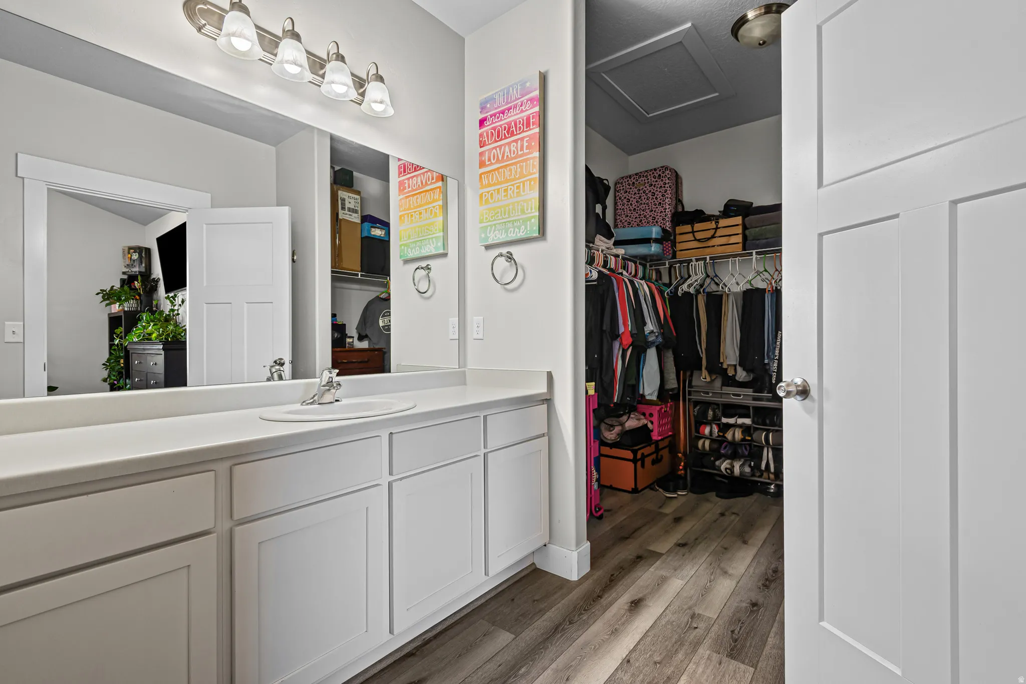 White vanity with an integrated sink and brushed nickel hardware, expansive vanity mirror, and wood-finish flooring