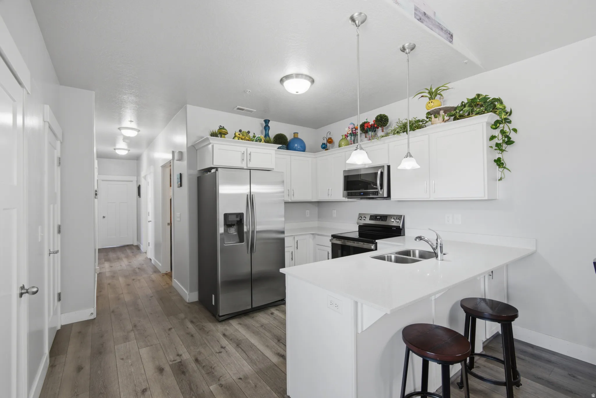 Kitchen featuring white cabinetry, stainless steel appliances, white countertops, a double basin sink, and wood-finish flooring