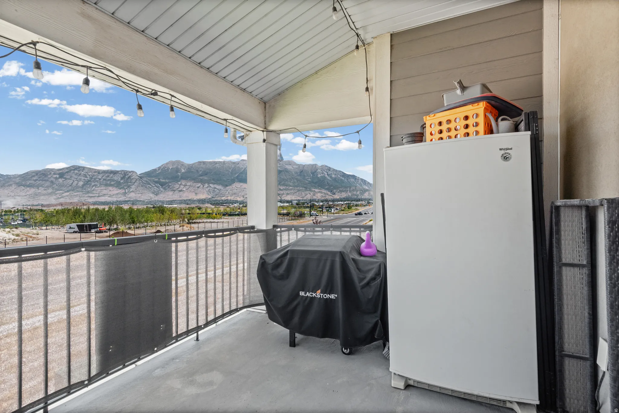 Covered balcony with concrete flooring, white support columns, and wrought iron railing