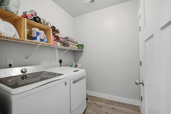 Dedicated laundry room featuring side-by-side washer and dryer appliances, wire shelving with ample storage capacity, wood-finish upper cabinetry, and wood-look plank flooring throughout