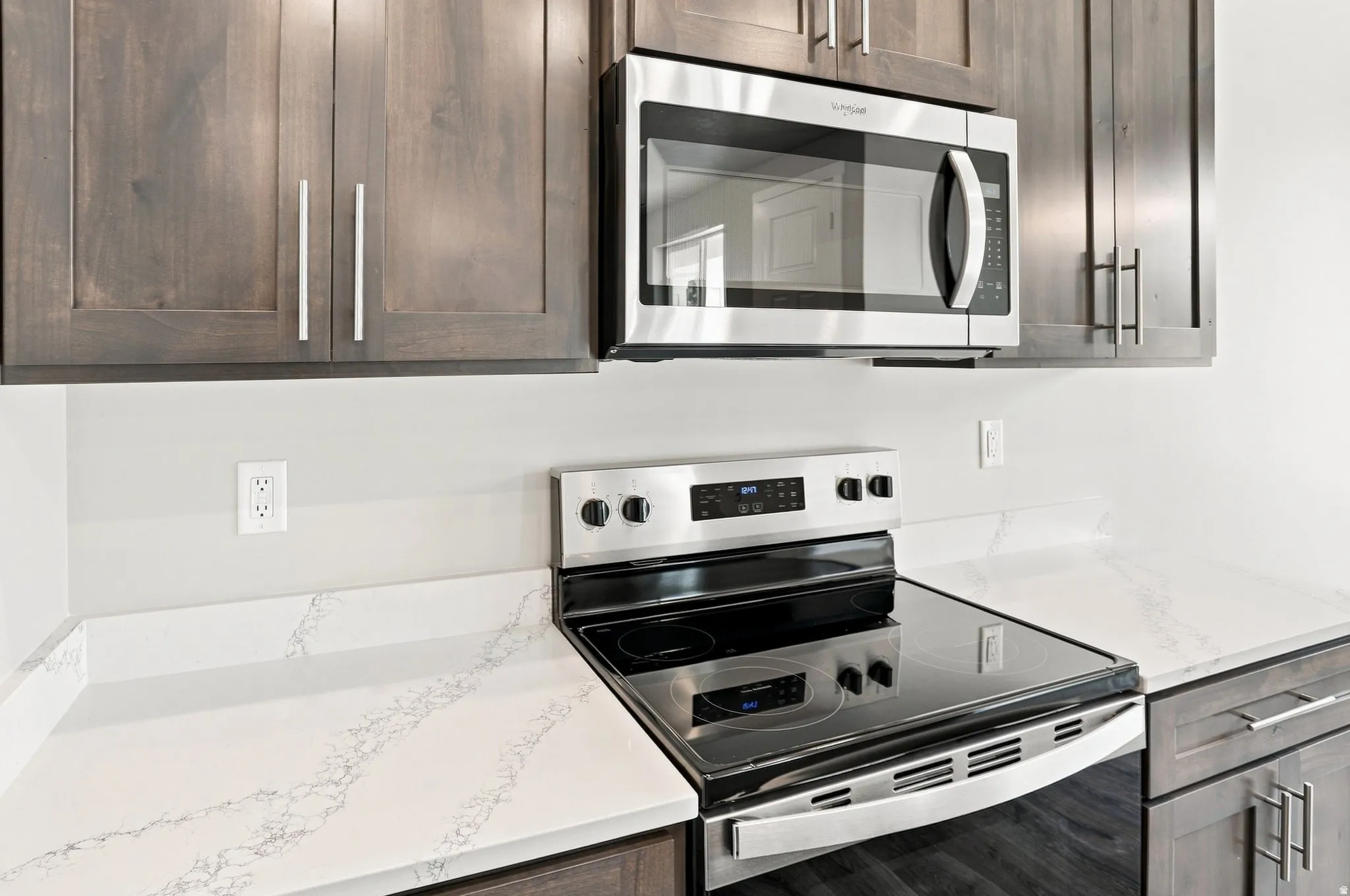 Stainless steel microwave, electric range, wood-finish cabinetry with bar pull hardware, and veined countertops