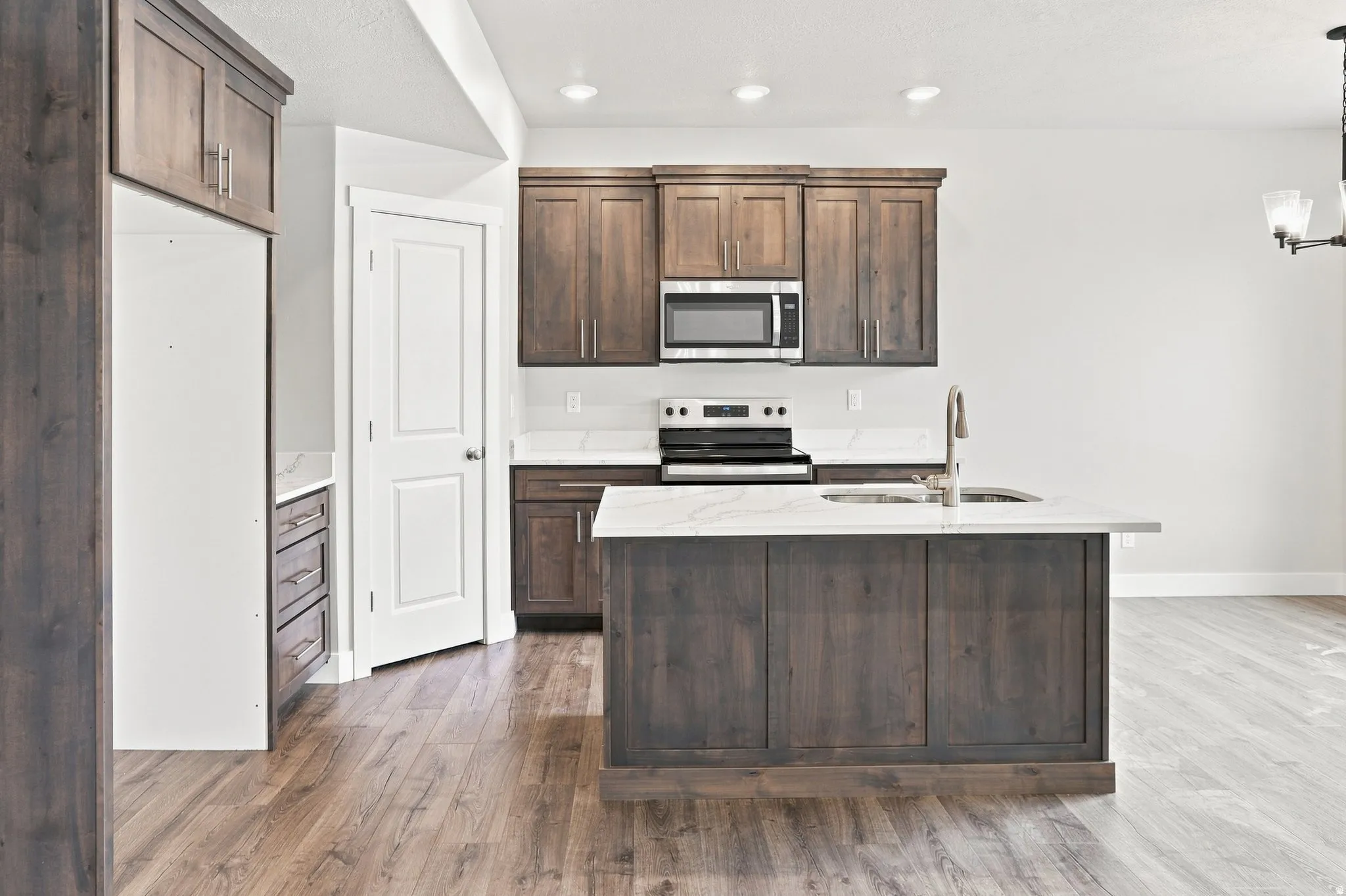 Kitchen with wood-finish flooring, dark wood cabinetry, white countertops, stainless steel microwave, and integrated sink