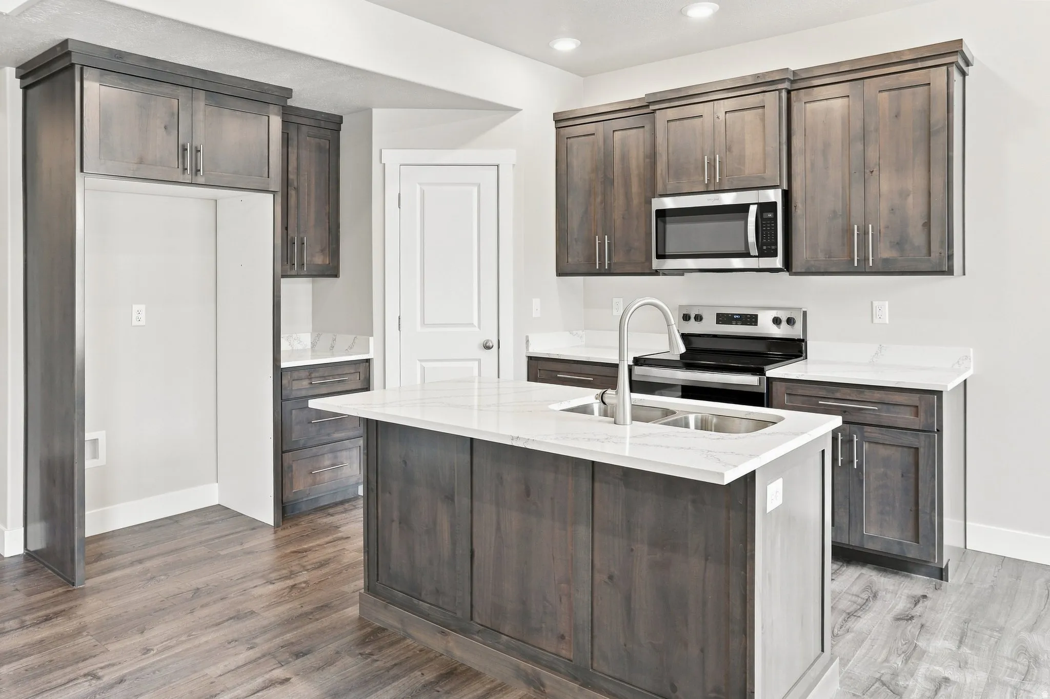 Kitchen featuring dark wood-finish cabinetry, light stone countertops, a stainless steel microwave, and a stainless steel double basin sink
