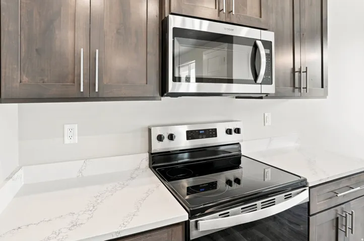 Stainless steel microwave, electric range, wood-finish cabinetry with bar pull hardware, and veined countertops