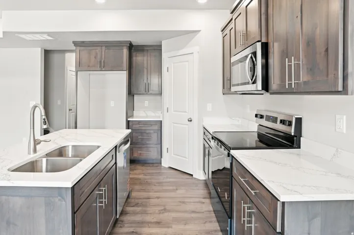 Spacious kitchen featuring an island with a double basin sink, white countertops, wood-finish flooring, and built-in stainless steel appliances