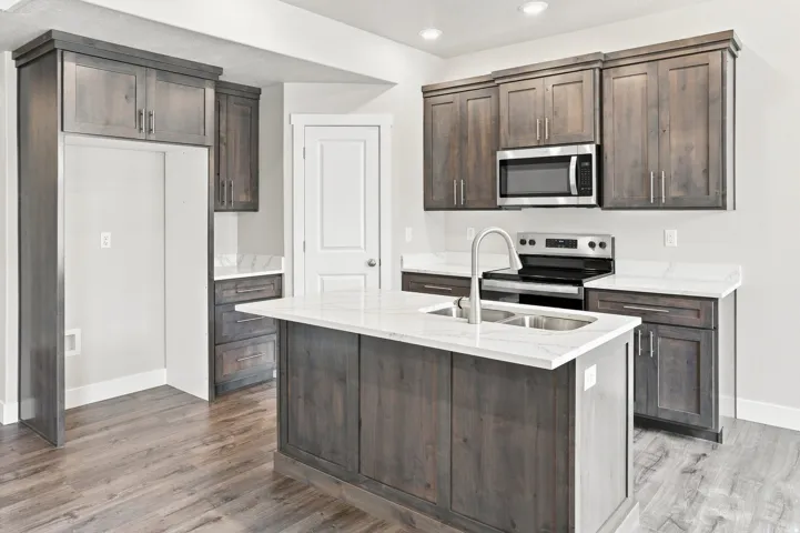 Kitchen featuring dark wood-finish cabinetry, light stone countertops, a stainless steel microwave, and a stainless steel double basin sink