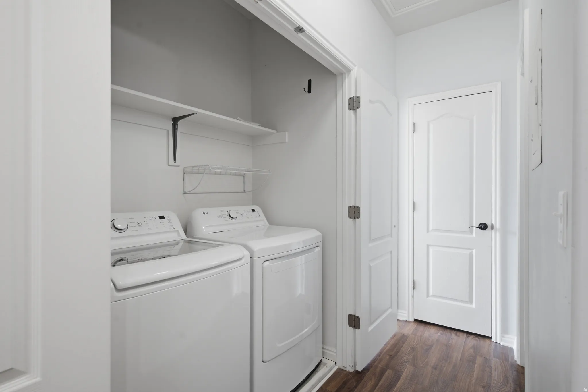 Dedicated laundry area featuring a washer and dryer, an overhead shelf for storage, and wood-finish flooring