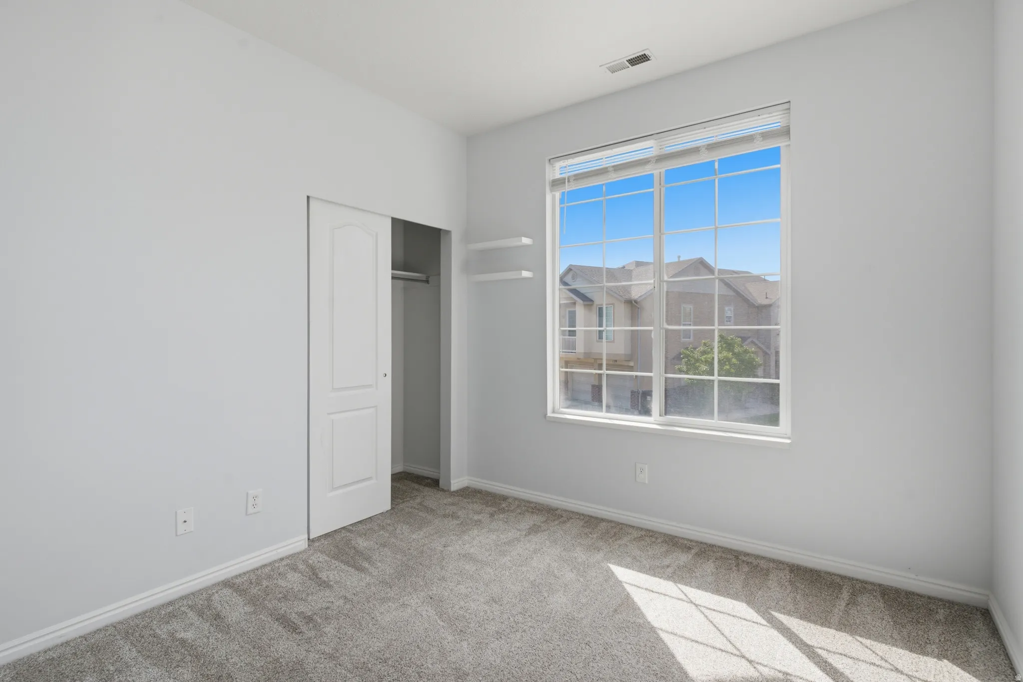 Neutral wall finish, window with grid panes, wall-mounted shelving, closet with bi-fold door, and carpet flooring