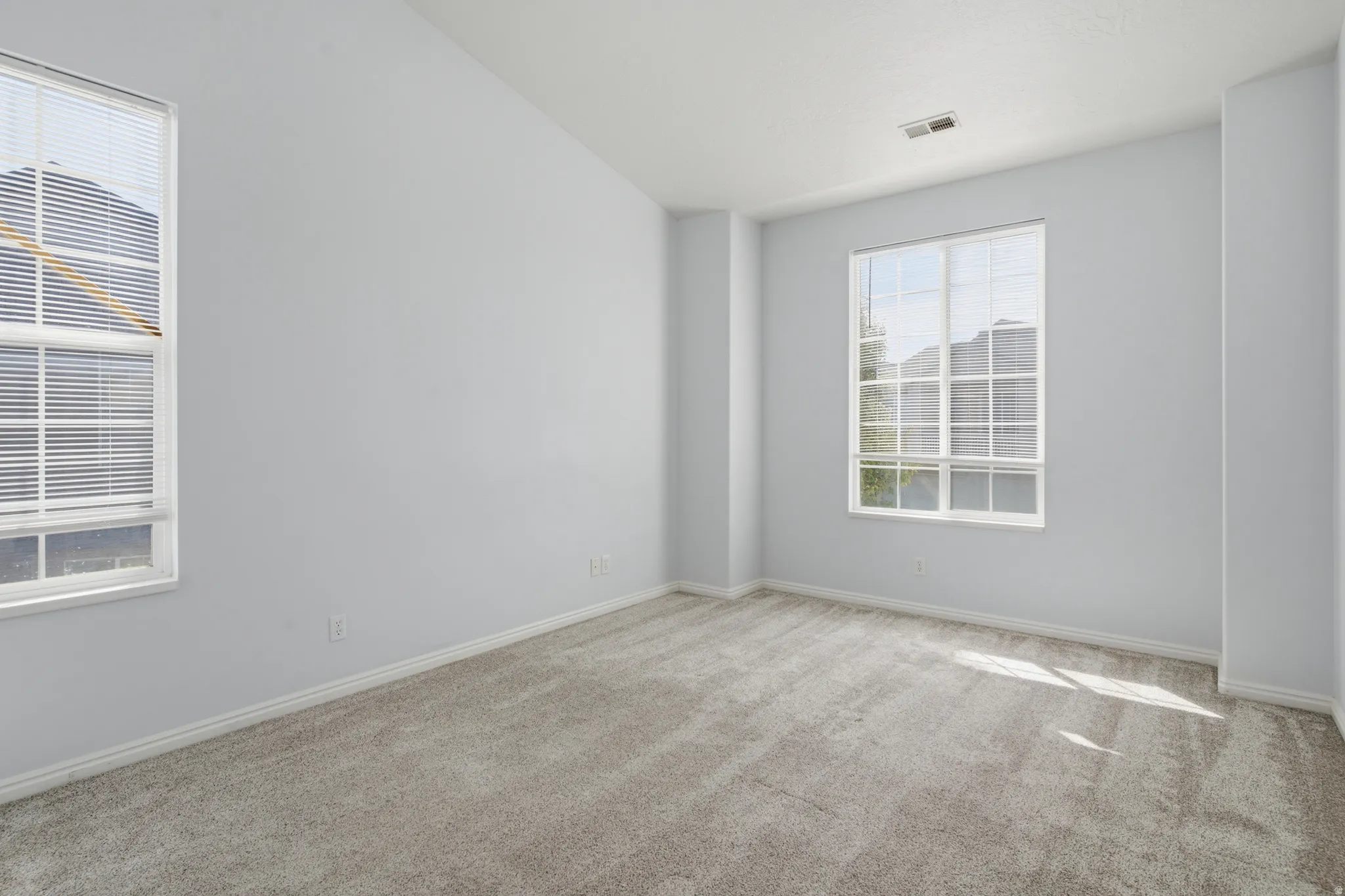 Vaulted ceiling with gray carpeting and two large windows