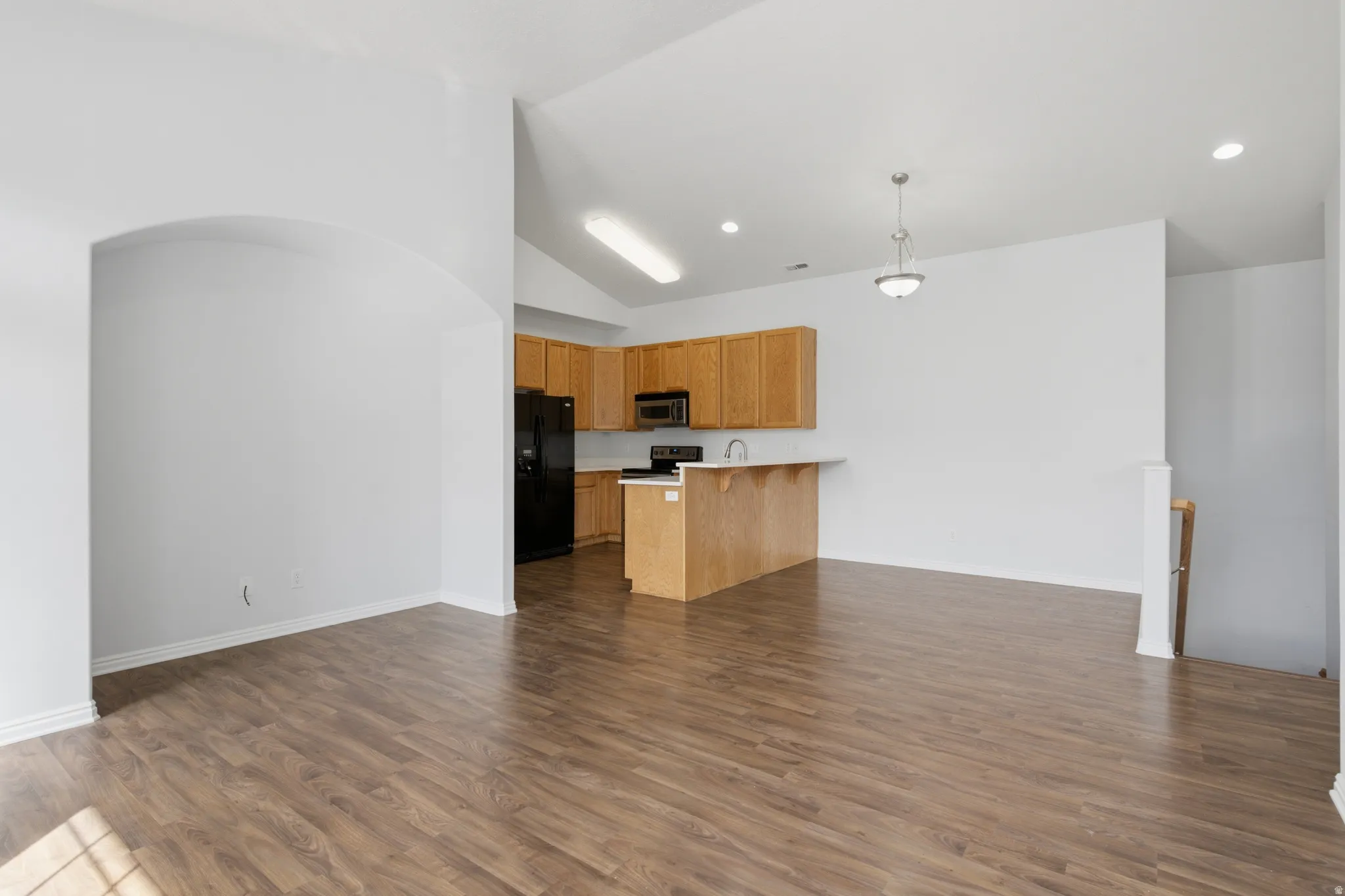 Vaulted ceiling, recessed lighting, wood-finish flooring, breakfast bar, and wood cabinetry