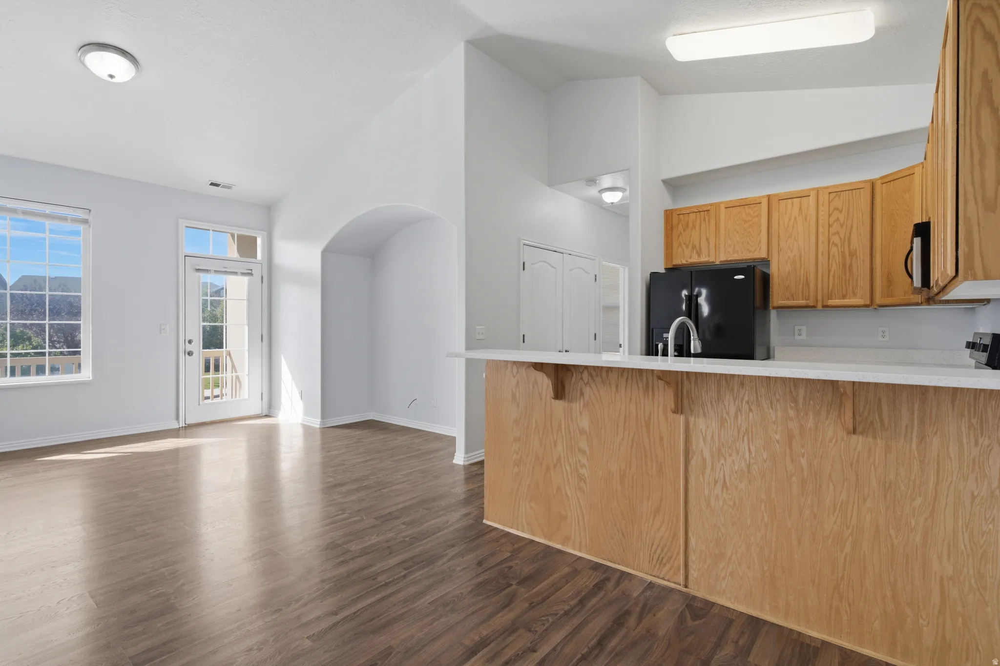 Wood-finish flooring, white walls, arched doorway, light wood cabinetry, and a built-in breakfast bar