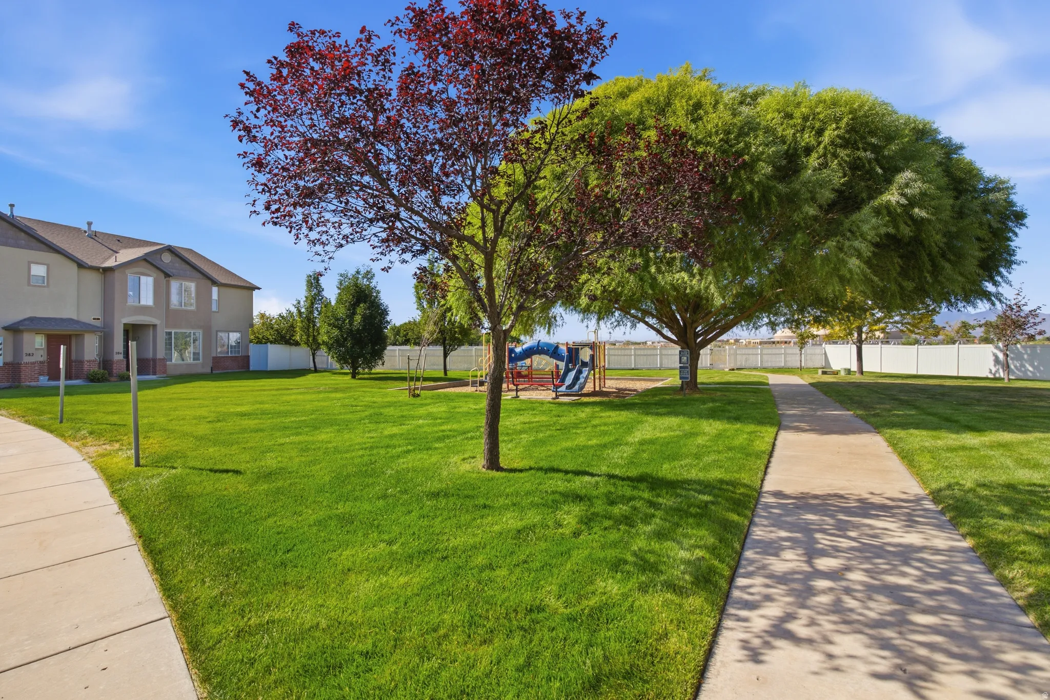 Expansive green space featuring mature trees, a playground, and paved pathways