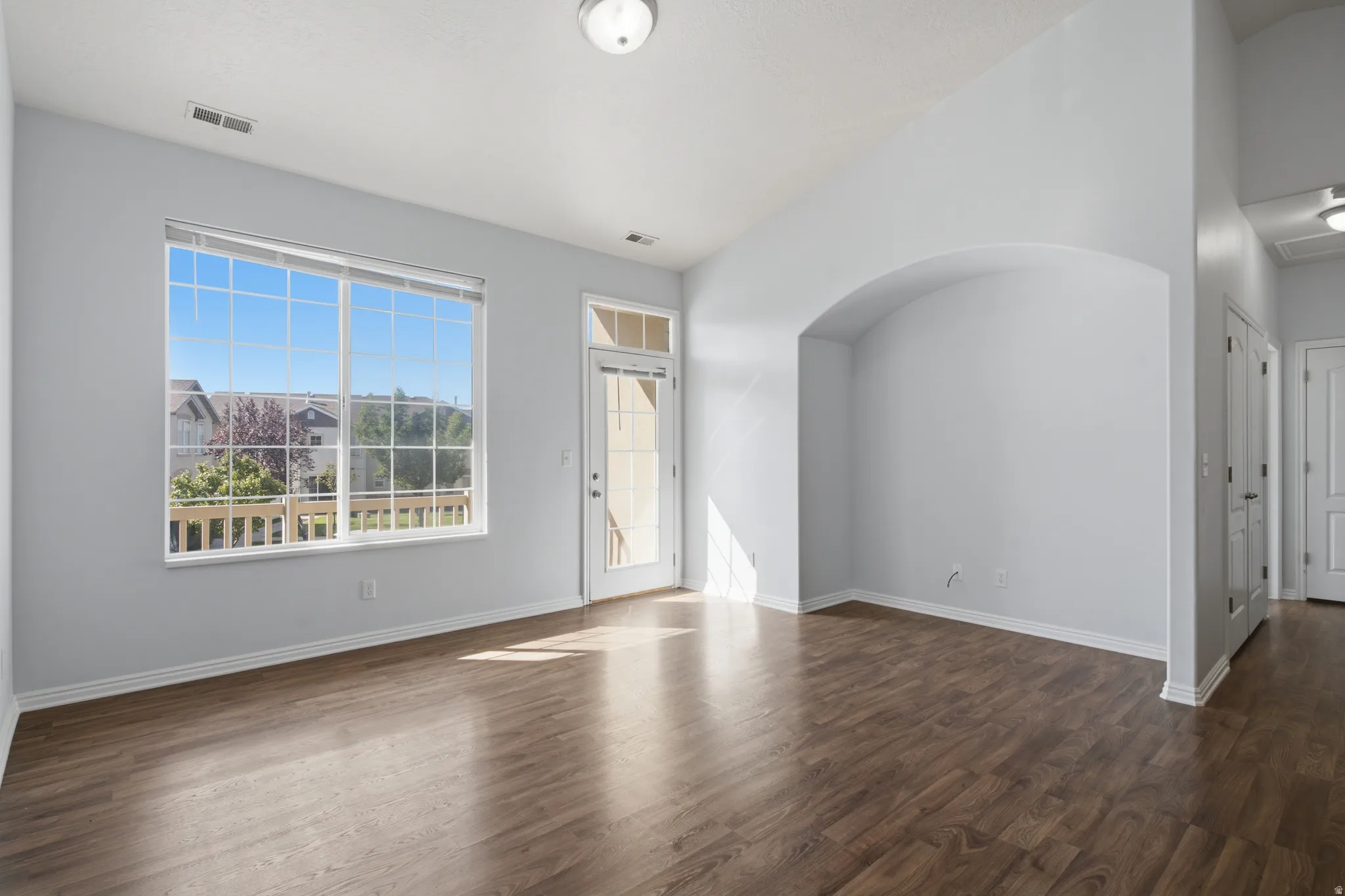 Expansive window, patio door, wood-finish flooring, vaulted ceiling, and an arched alcove