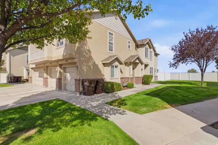 Multi-story stucco exterior with brick accents, individual attached garages, mature landscaping, and a fenced perimeter