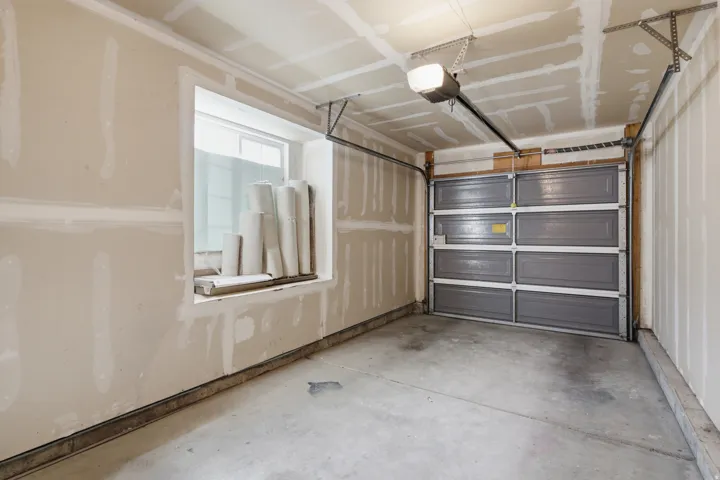 Garage with an automatic opener, grey sectional garage door, concrete flooring, and a single window
