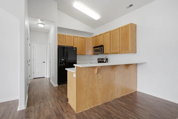 Kitchen featuring light wood-finish cabinetry, black and stainless steel appliances, a breakfast bar, and wood-finish flooring