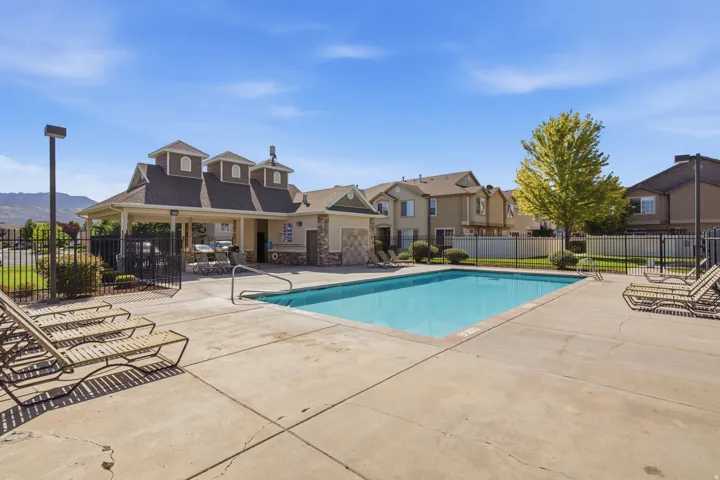 Outdoor community swimming pool with concrete decking, surrounding black metal fencing, and an adjacent covered structure with stone accents