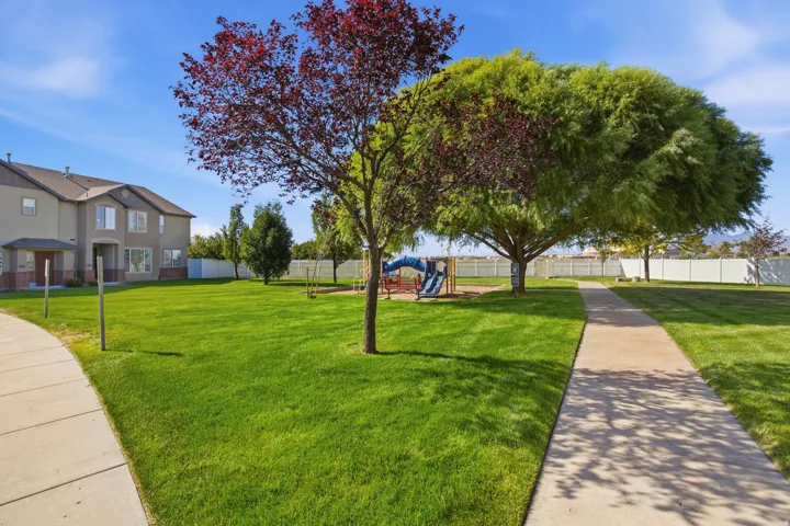 Expansive green space featuring mature trees, a playground, and paved pathways