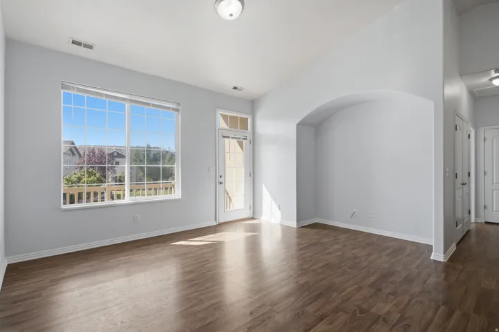 Expansive window, patio door, wood-finish flooring, vaulted ceiling, and an arched alcove