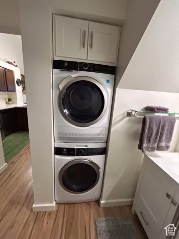 Stackable washer and dryer, white shaker-style cabinetry with brushed nickel hardware, and wood-finish flooring