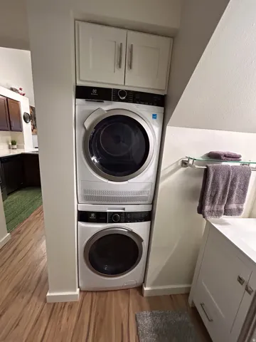 Stackable washer and dryer, white shaker-style cabinetry with brushed nickel hardware, and wood-finish flooring