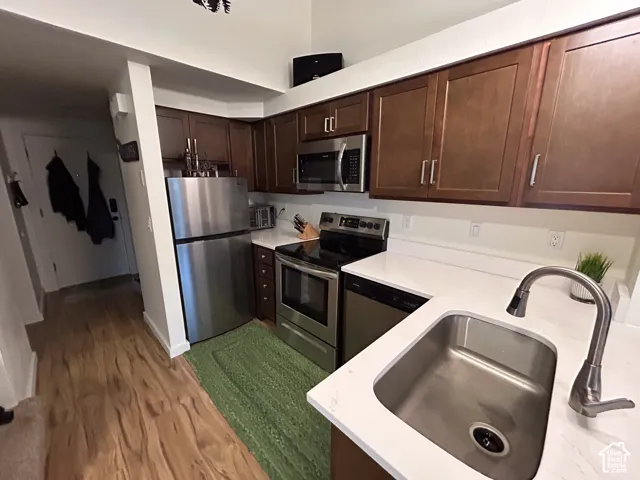 Kitchen featuring wood-finish flooring, stainless steel appliances, white countertops, and wood-finish cabinetry