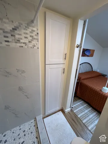 Shower with marble-look tile, pebble mosaic floor, and white shaker-style cabinetry