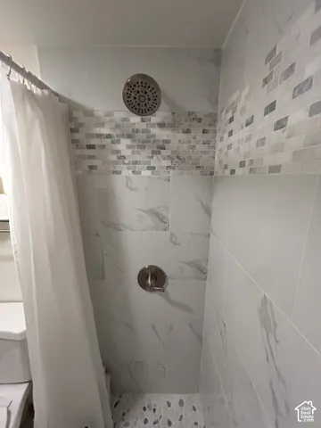 Shower with large format wall tiles, a decorative mosaic tile band, pebble-finish flooring, and a brushed nickel showerhead