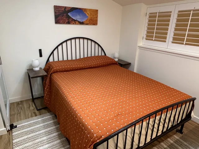 Wood-finish flooring, white plantation shutters, and a streamlined metal bed frame
