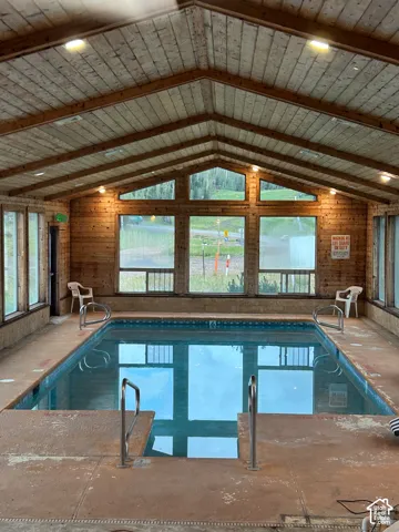 Indoor swimming pool with wood-paneled walls and ceiling, large windows, and recessed lighting