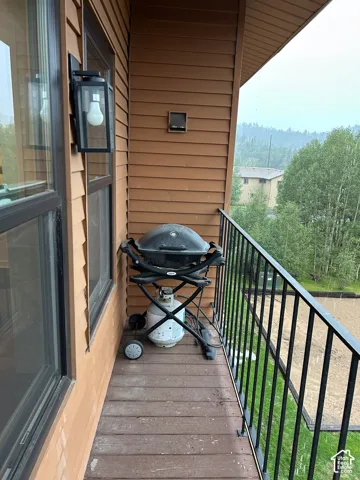 Balcony with wood-finish decking, black metal railing, and wall-mounted exterior lighting