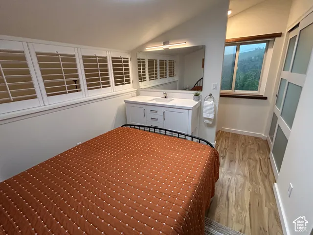 Angled ceiling with track lighting, white vanity with integrated sink, large wall-mounted mirror, white plantation shutters, and wood-finish flooring
