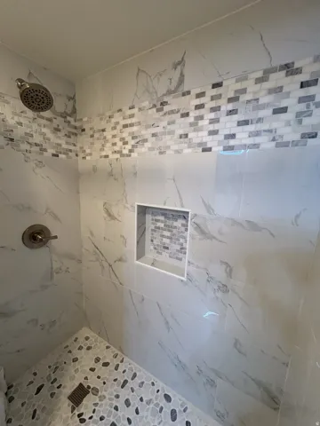 Shower featuring large-format stone-finish wall tile, decorative mosaic tile band, and a built-in shower niche