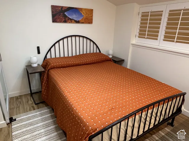 Wood-finish flooring, white plantation shutters, and a streamlined metal bed frame