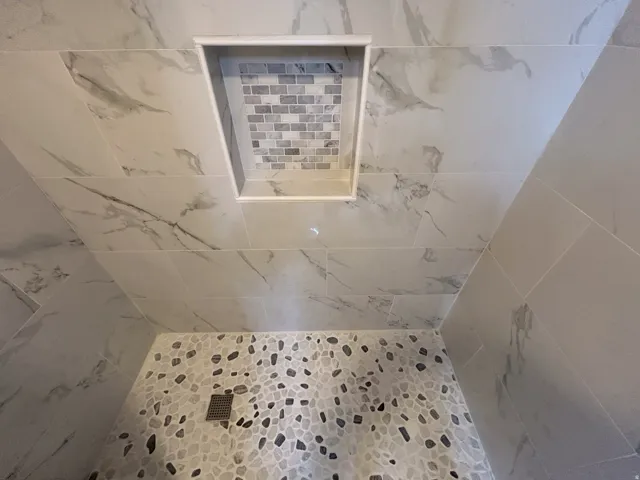Shower featuring large format wall tile with a marble-effect pattern, a mosaic tile niche, and a pebble-style floor