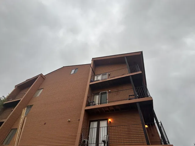 Multi-level exterior with horizontal wood-finish siding, multiple balconies with black metal railings, and integrated wall sconces
