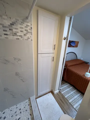Shower with marble-look tile, pebble mosaic floor, and white shaker-style cabinetry