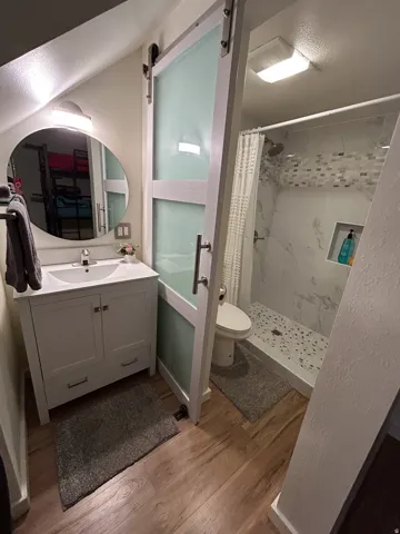 Wood-finish flooring with a white vanity and circular mirror