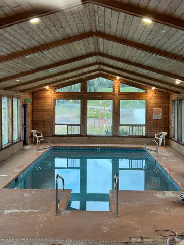 Indoor swimming pool with wood-paneled walls and ceiling, large windows, and recessed lighting