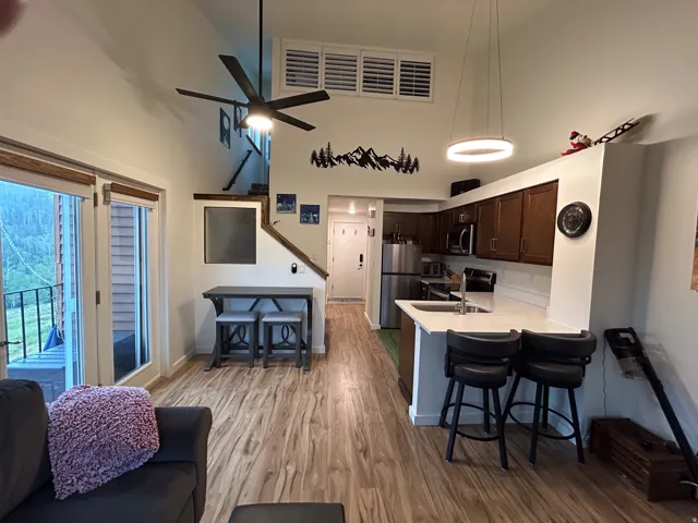 Vaulted ceiling with a ceiling fan, wood-finish flooring, kitchen with stainless steel appliances, white countertops, and wood cabinetry, and a glass-paneled door