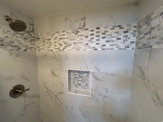 Shower with large format tile, mosaic accent band, built-in niche, and brushed nickel fixtures