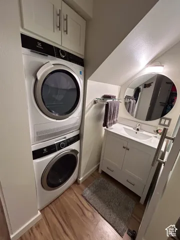 Stacked washer and dryer, wood-finish flooring, white vanity with integrated sink, wall-mounted oval mirror, and built-in upper cabinetry