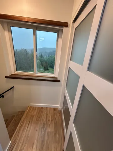Wood-finish flooring, sliding door with frosted glass panels, wood window trim, and a black handrail